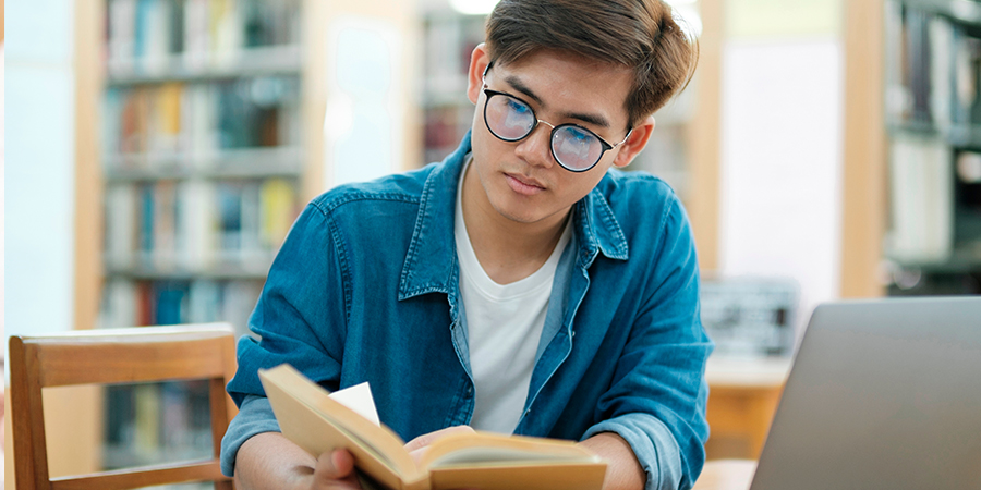 Um estudante sentado lendo um livro na biblioteca da escola