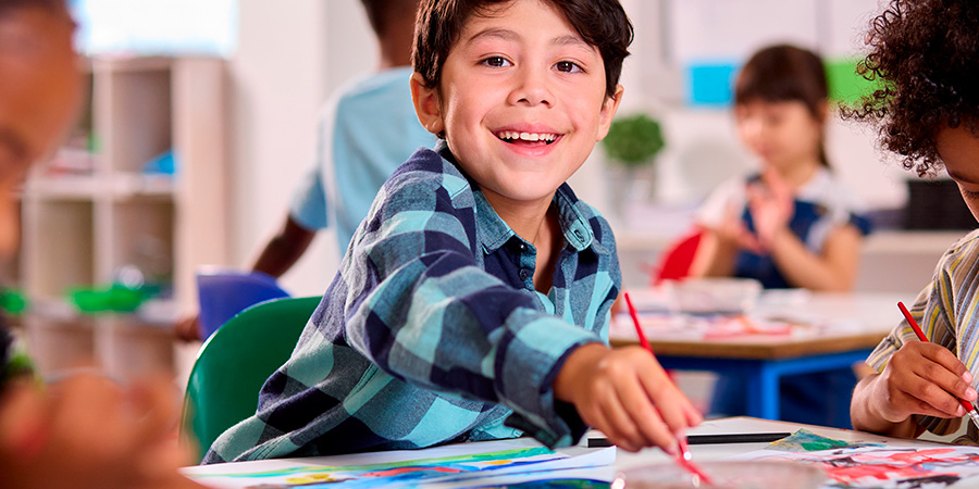 menino sorrindo na escola fazendo artes manuais 